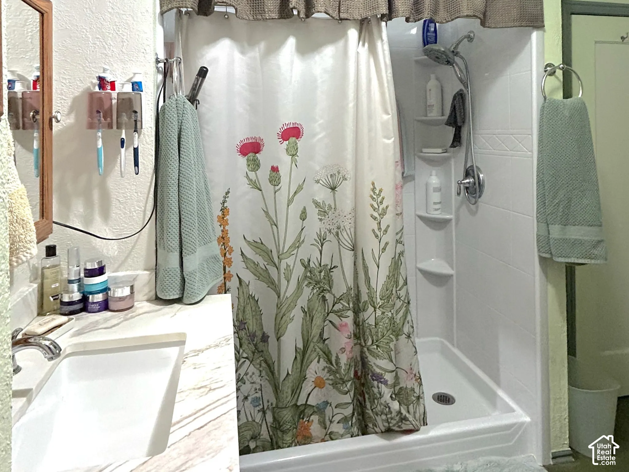 Vanity with an integrated sink and a light-toned countertop, a walk-in shower stall with built-in shelving, and tiled flooring