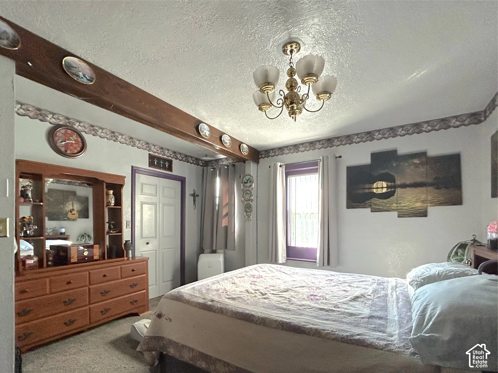 Ceiling-mounted chandelier fixture, white paneled bifold doors, window with purple trim, decorative ceiling beam, and textured ceiling
