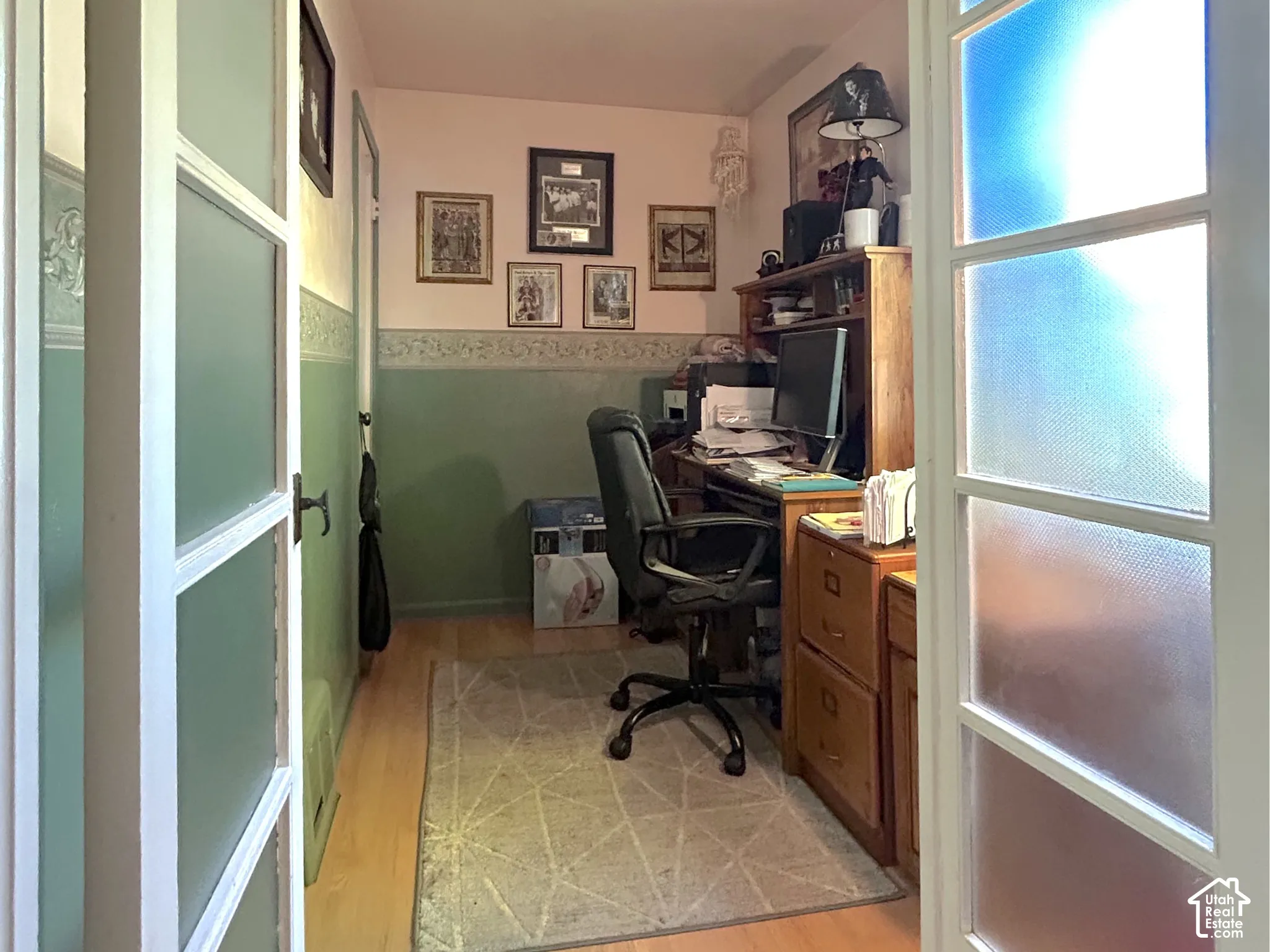 French doors with frosted glass panels open to an office featuring wood-finish flooring and a flush-mount ceiling light fixture