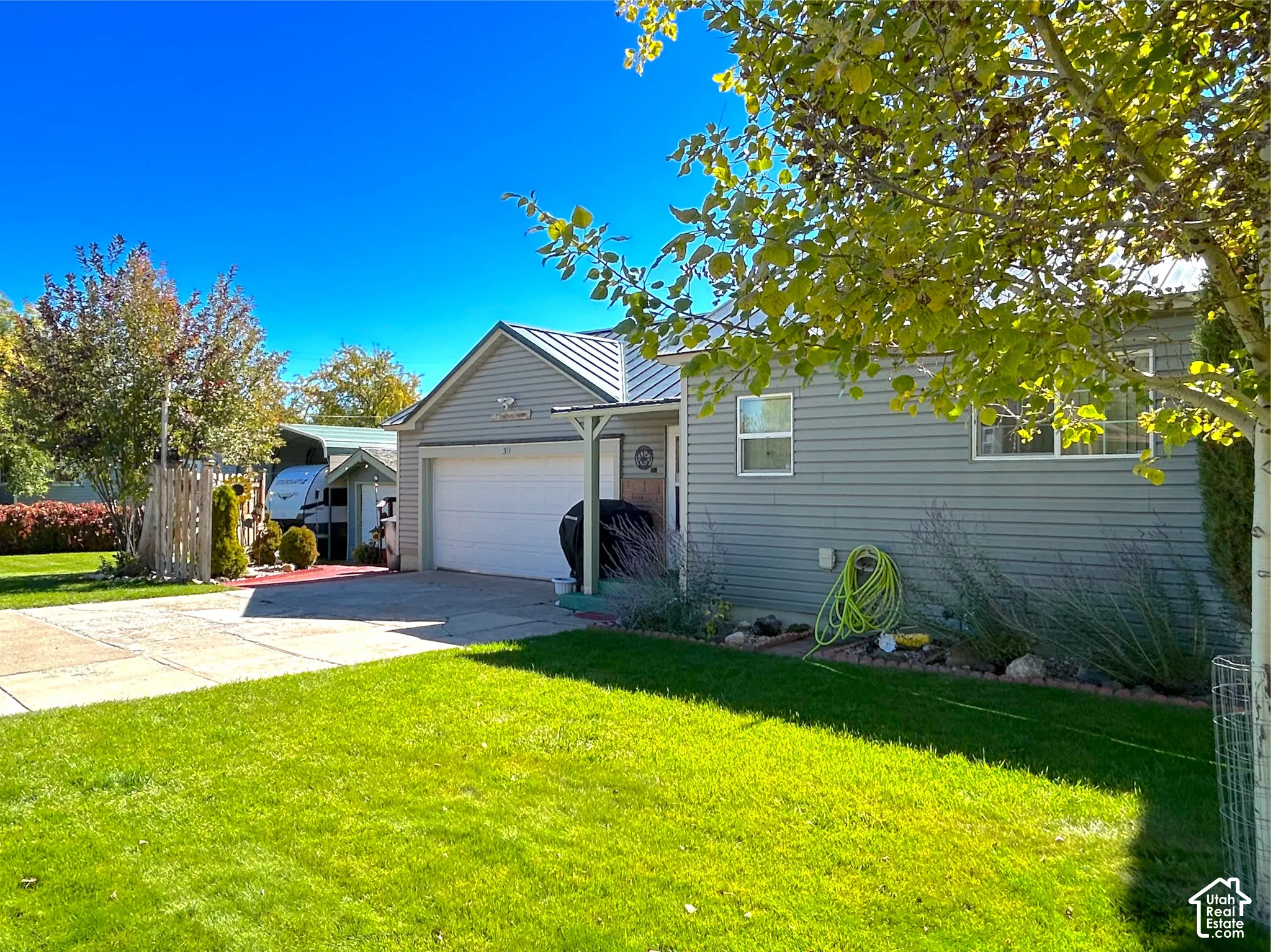 Exterior featuring gray horizontal siding, an attached garage with a white door, a metal roof, and a paved driveway