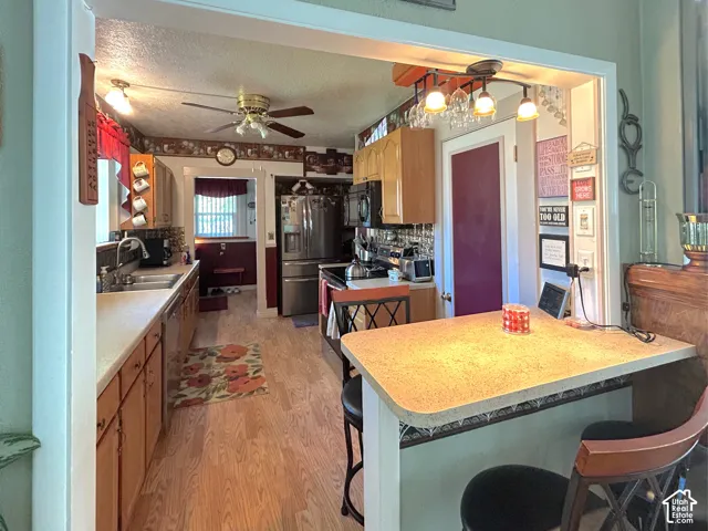 Wood-finish flooring throughout the kitchen, featuring light wood-finish cabinetry, a double basin sink, and stainless steel appliances