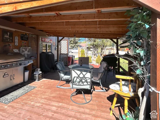 Covered wooden deck with exposed beam ceiling, stainless steel grill, and lattice privacy screen