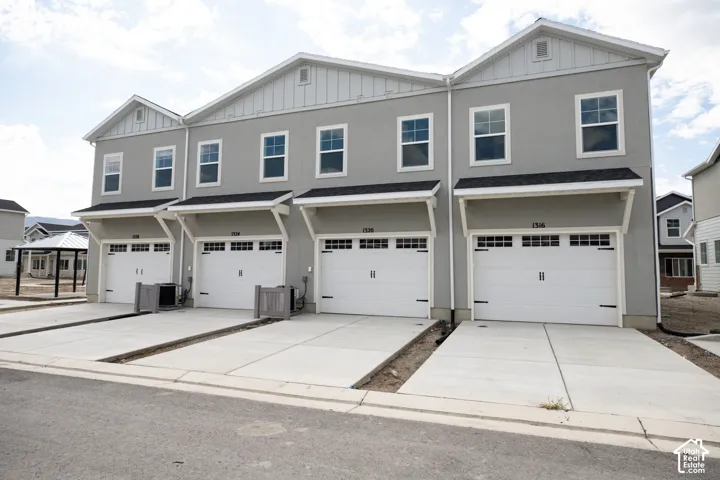 Rear view of townhome with garage and extended driveway for additional parking.