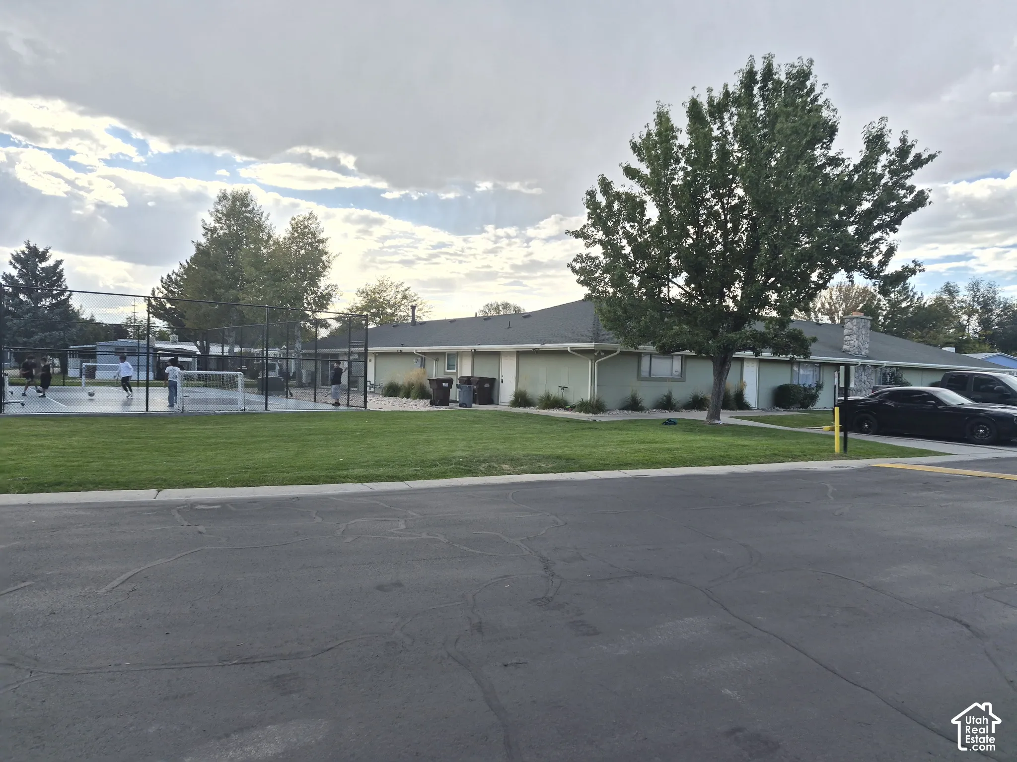 Expansive green space featuring a multi-sport court with surrounding fencing, a manicured lawn, and mature trees