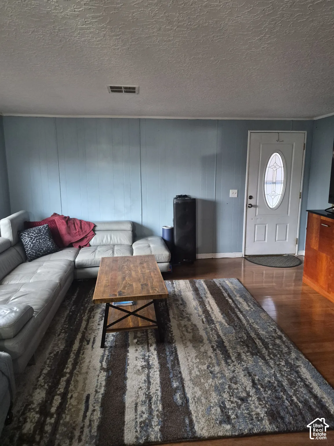 Hardwood flooring, light blue paneled walls, and a white entry door with an oval window