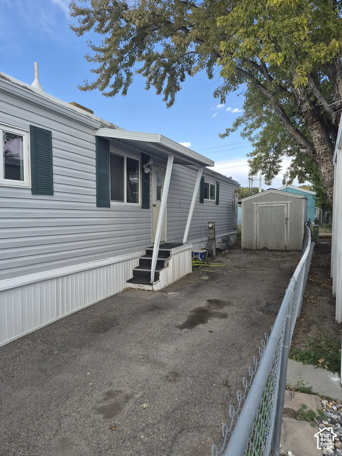 Gray siding exterior with dark green shutters, covered entry with steps, and a detached storage shed