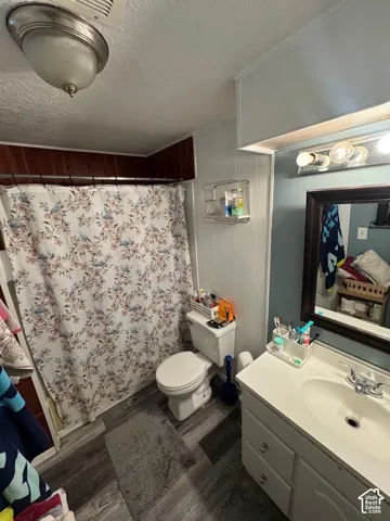 Bathroom featuring wood-finish flooring, a white vanity with an integrated basin, a wall-mounted wire shelf, and a shower area with wood-paneled walls