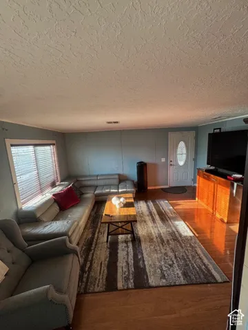 Living area featuring wood-finish flooring, textured ceiling, and an entry door with an oval glass inset