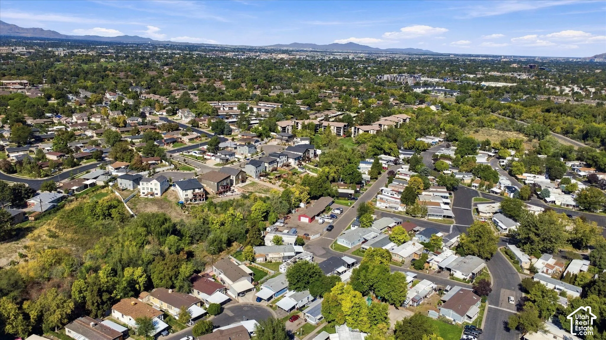 Expansive residential area featuring a mix of housing styles, mature trees, paved streets, and distant mountain ranges
