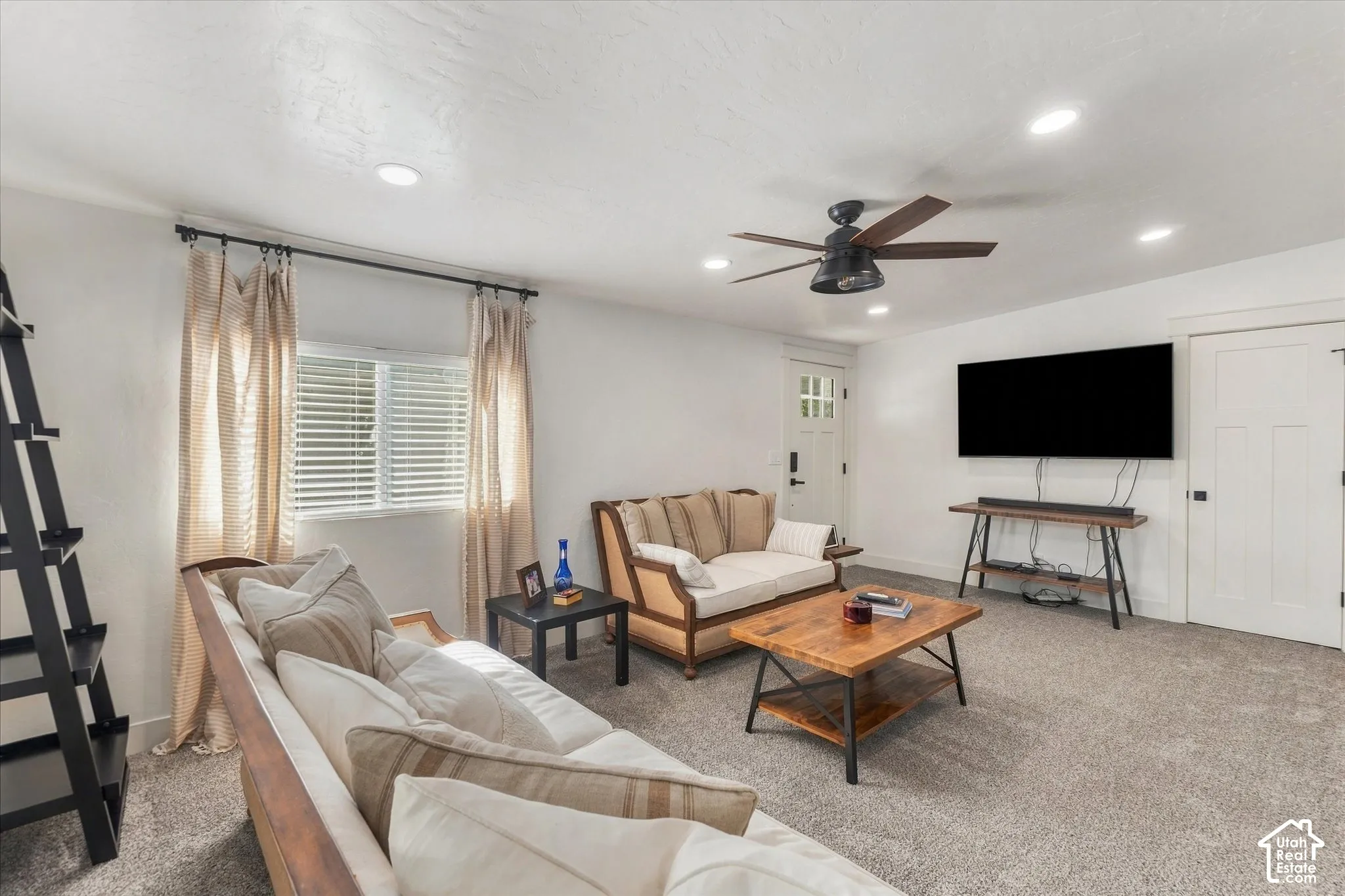 Carpeted living area with recessed lighting, a ceiling fan, and a window with blinds
