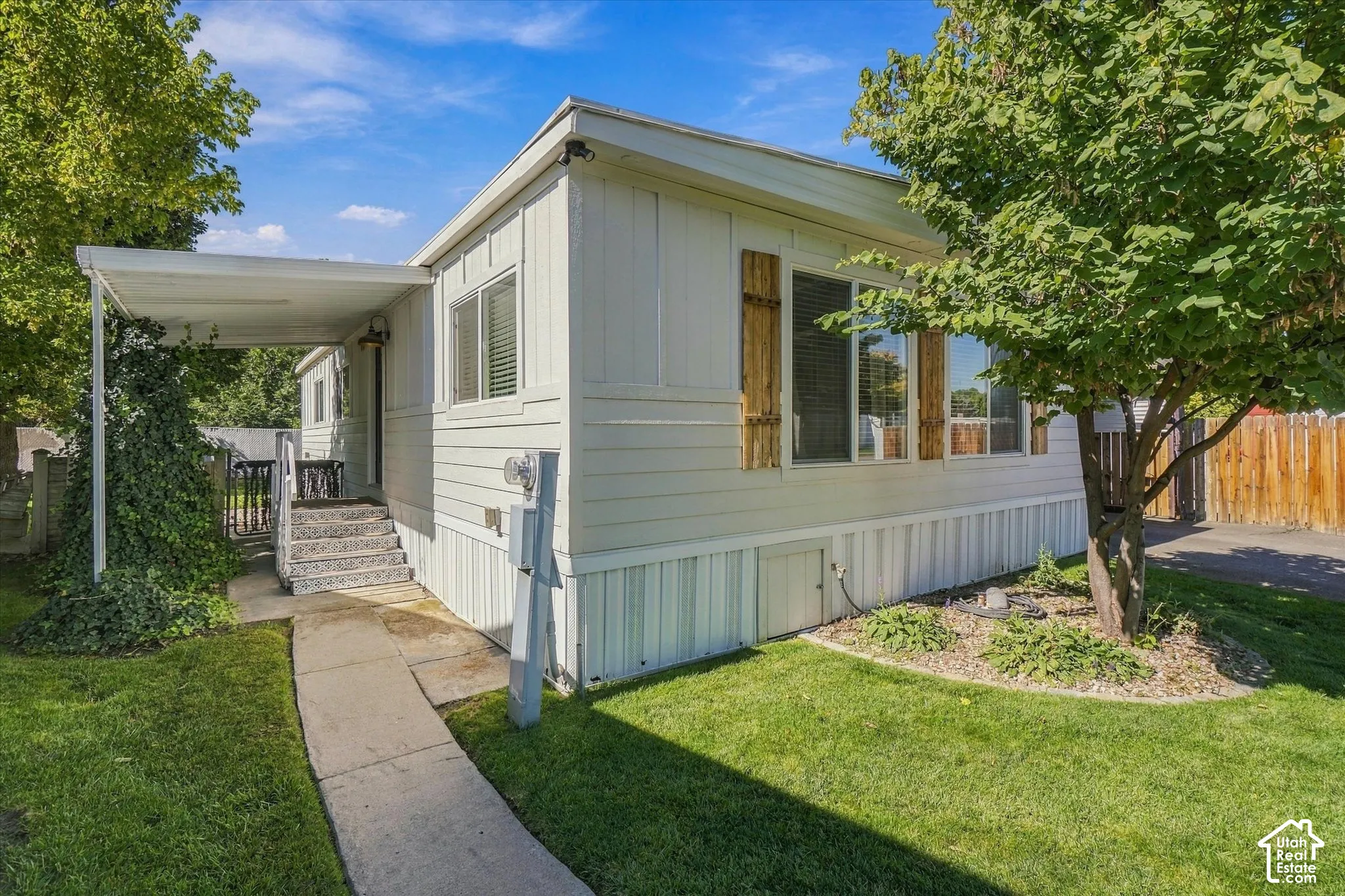 White siding exterior with a covered entry, wood-finish window shutters, and a paved walkway