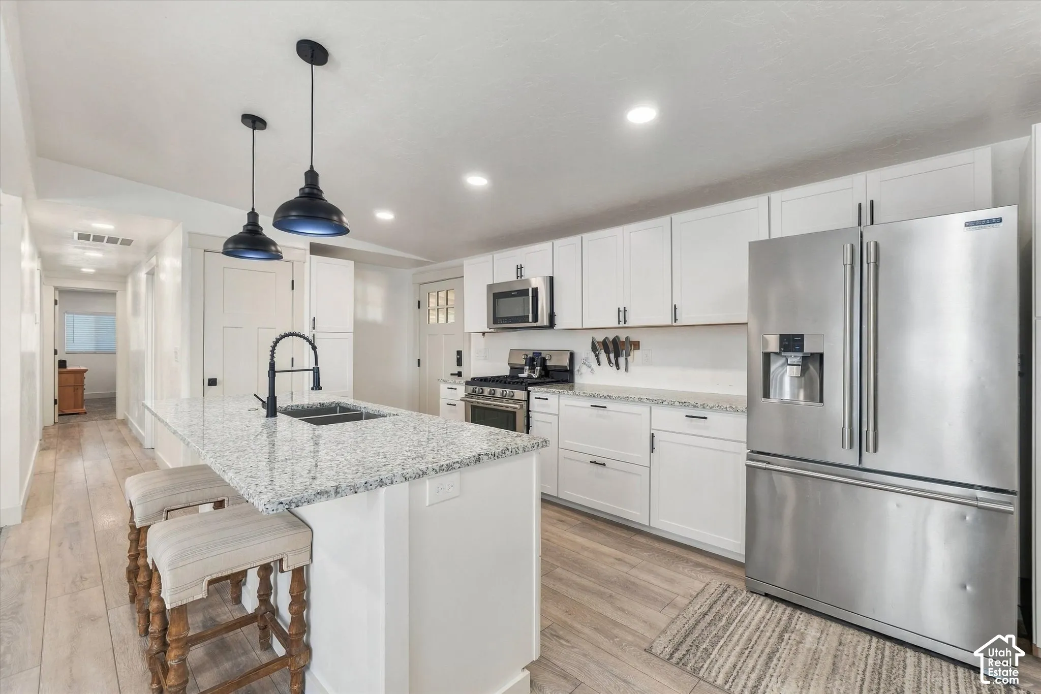 Kitchen featuring a center island with a built-in sink, white cabinetry with dark hardware, stainless steel appliances, recessed lighting, and wood-finish flooring