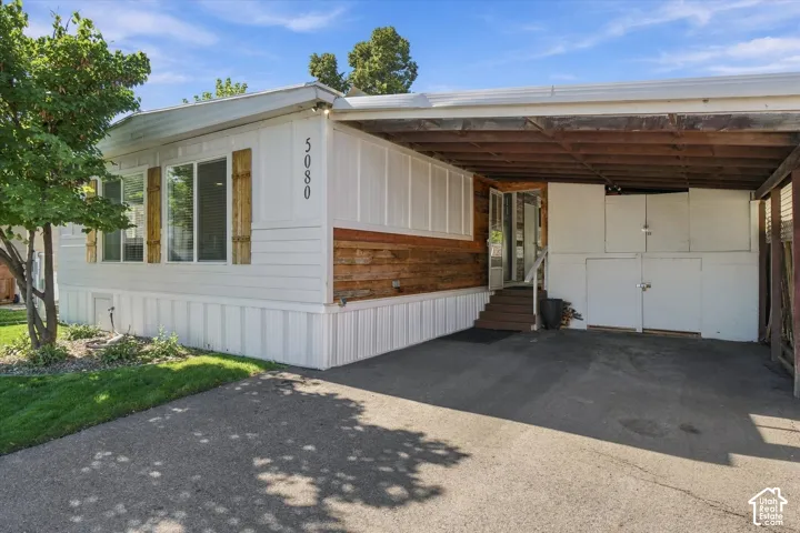 Covered carport with integrated storage, wood-paneled siding, and a paved driveway