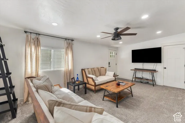 Carpeted living area with recessed lighting, a ceiling fan, and a window with blinds