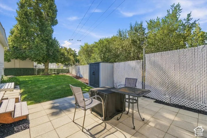 Paved patio with concrete pavers, privacy fencing, a storage shed, and a mature tree