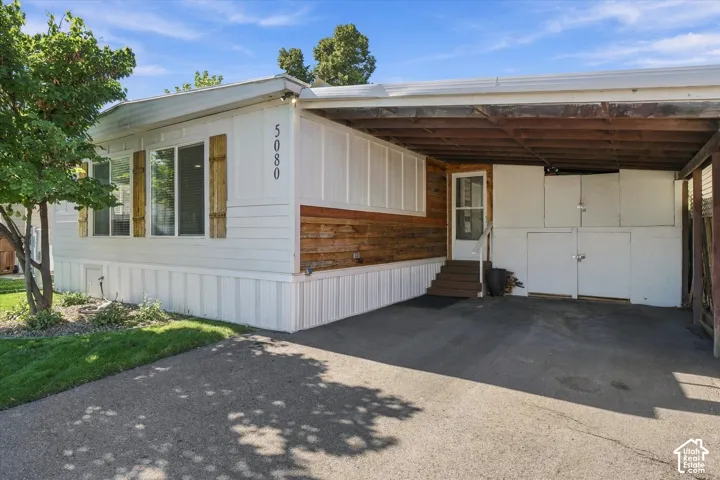 Exterior with horizontal white siding and wood-finish accent panels, featuring a covered carport and numerical address display
