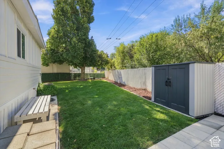 Grassed yard with a privacy fence, mature trees, and a storage shed