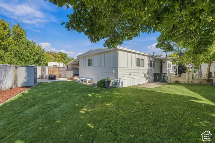 Expansive green lawn, mature trees, white vertical panel siding, concrete patio, and a chain-link fence