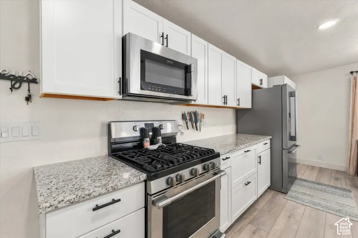 Kitchen featuring white shaker cabinetry, stainless steel appliances, speckled countertops, and wood-finish flooring