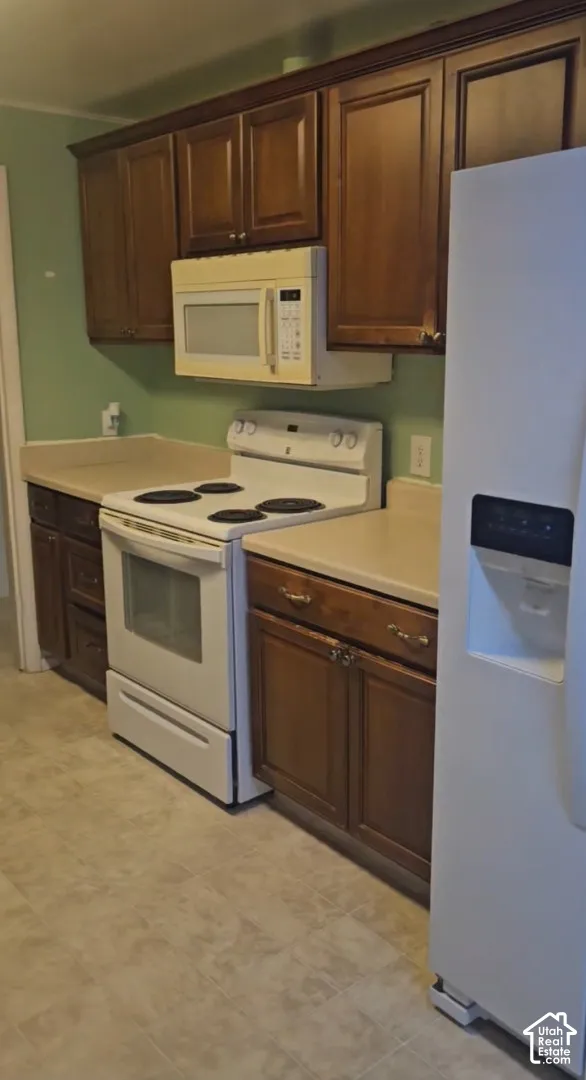 Wood-finish cabinetry, light-toned countertops, white range, white microwave, and vinyl flooring