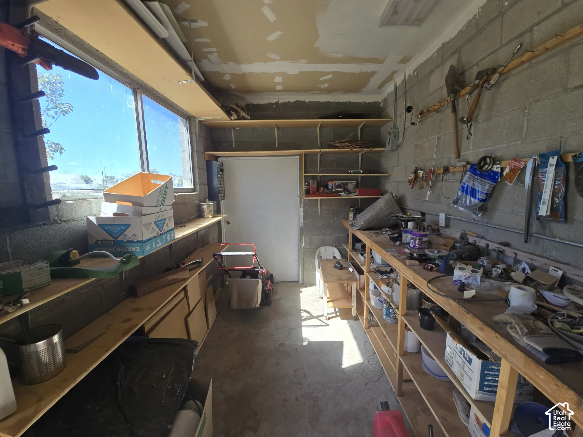 Concrete block walls with extensive built-in shelving, a full-length workbench, and natural light from a prominent window