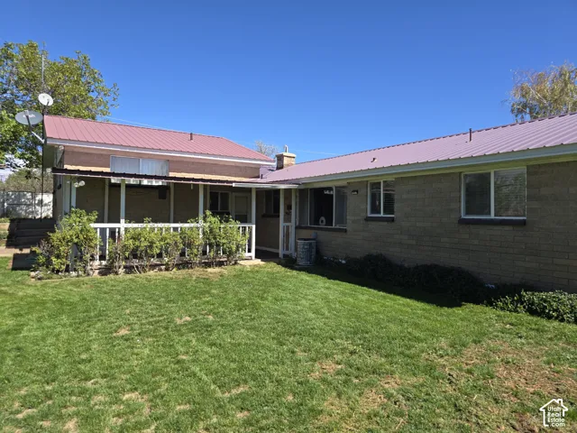 Metal roof, brick exterior, covered patio with white railing, and a grass lawn