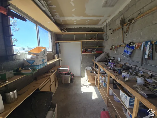 Concrete block walls with extensive built-in shelving, a full-length workbench, and natural light from a prominent window