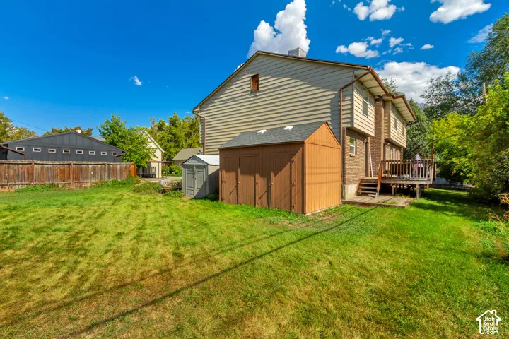 Expansive backyard with a wooden fence, two storage sheds, and a raised wood deck with railing