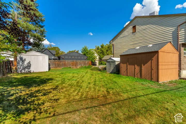 Expansive backyard featuring a manicured lawn, mature shade trees, and wooden storage structures