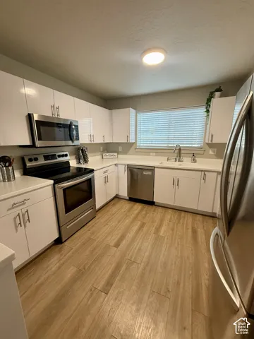 Kitchen featuring white cabinetry, stainless steel appliances, light-toned wood-finish flooring, and a window with blinds
