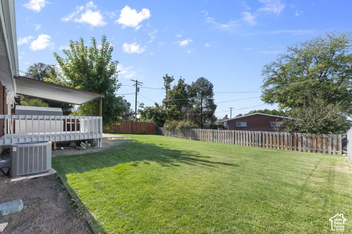 Spacious backyard with a covered patio deck, mature trees, and wood fencing