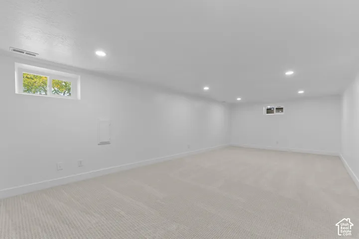 Spacious room with white walls, recessed lighting, and light-colored carpeting