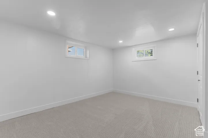 Recessed lighting illuminates a carpeted room featuring white paneling and two windows