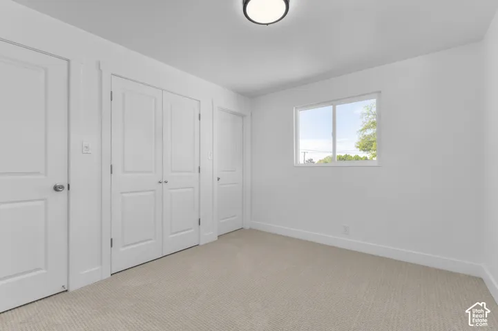 Neutral-toned carpeting complements the white walls and trim, with a single window providing natural illumination