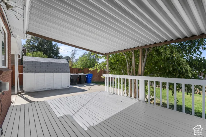 Expansive covered deck with white railing, concrete patio, and a storage shed