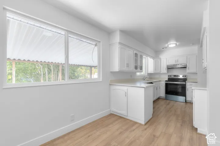 White cabinetry with glass-front accents, wood-finish flooring, stainless steel range, built-in stainless steel microwave, and white countertops