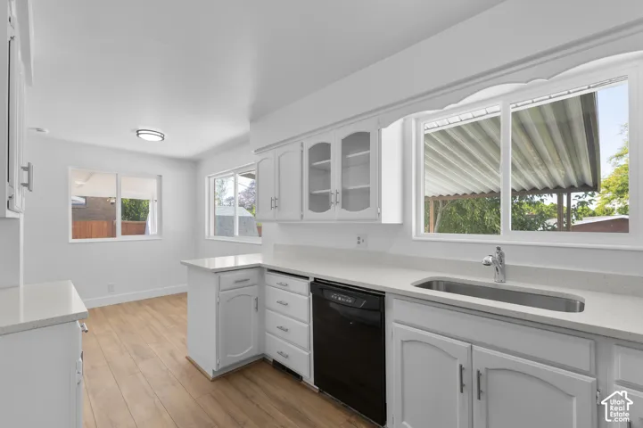 White cabinetry with silver hardware, light-toned countertops, integrated stainless steel sink with single-handle faucet, black dishwasher, and wood-finish flooring