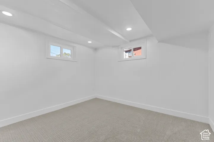 Recessed lighting, exposed ceiling beams, two windows, carpet flooring, and white wall paneling