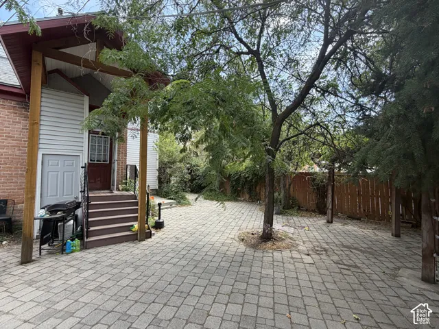 Paved patio with mature trees, brick and siding exterior, covered porch, and wood privacy fencing
