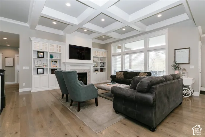 Coffered ceiling with recessed lighting, integrated built-in cabinetry, wood-finish flooring, fireplace with stone surround and mantel, and large picture windows