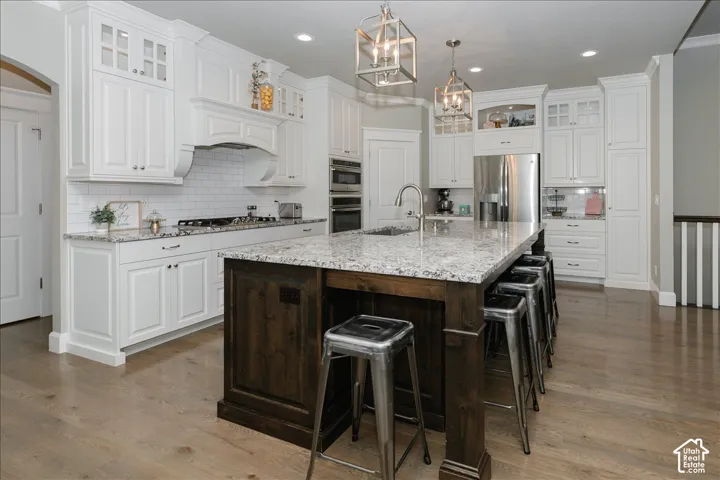 Spacious kitchen featuring an expansive center island, white cabinetry, integrated stainless steel appliances, wood-finish flooring, and subway tile backsplash