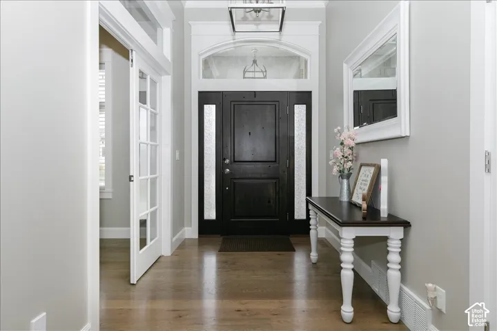 Hardwood-style flooring throughout, dark wood entry door with frosted sidelights, arched transom window, white trim and crown molding, and white French doors