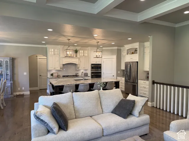Open-concept living space featuring a gourmet kitchen, coffered ceiling, wood-finish flooring, and a large kitchen island with seating