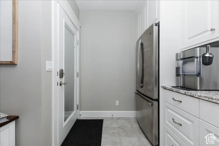 Stainless steel refrigerator, white cabinetry, integrated ice maker, solid surface countertop, tiled flooring