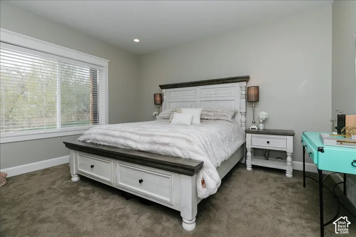Recessed ceiling lighting illuminates a spacious room featuring a large window with blinds and plush carpeting