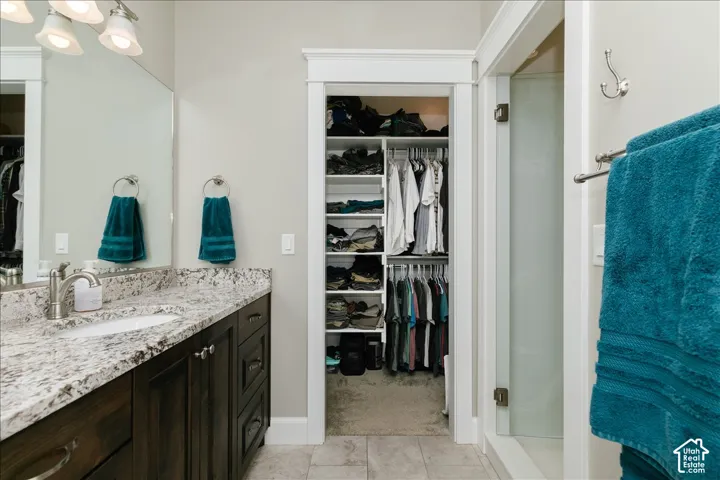 Vanity with stone countertop and undermount sink, brushed nickel faucet, large wall mirror, and overhead vanity lighting