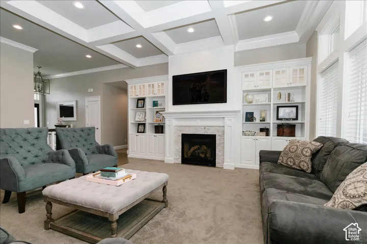Recessed lighting illuminating a coffered ceiling, a fireplace with stone surround and classic mantel, built-in cabinetry with glass-front uppers, and large windows with blinds