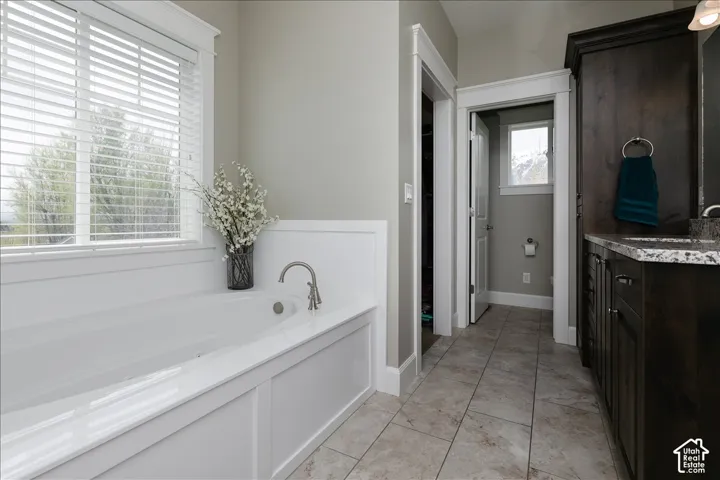 Soaking tub with brushed nickel fixtures, paneled wainscoting, tile flooring, and dark wood cabinetry with a light-colored countertop