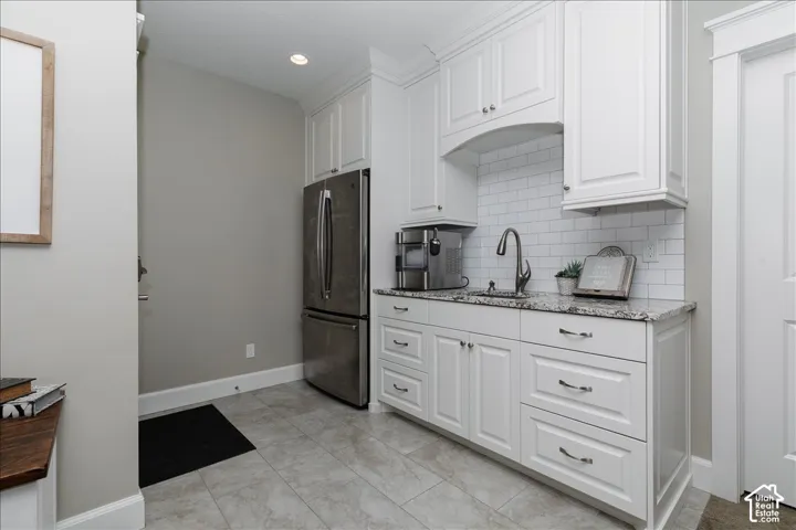White cabinetry with chrome hardware, subway tile backsplash, stainless steel refrigerator, and tiled flooring