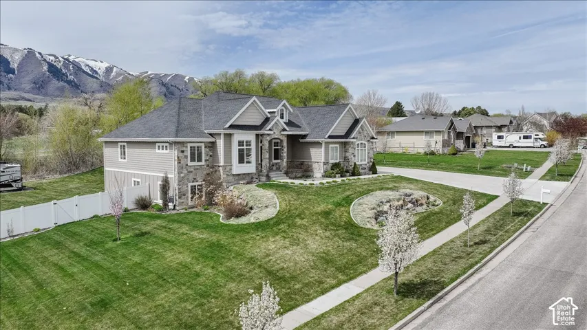 Stone and siding exterior with a dark shingle roof, featuring a landscaped front yard with a white fence, and a paved driveway